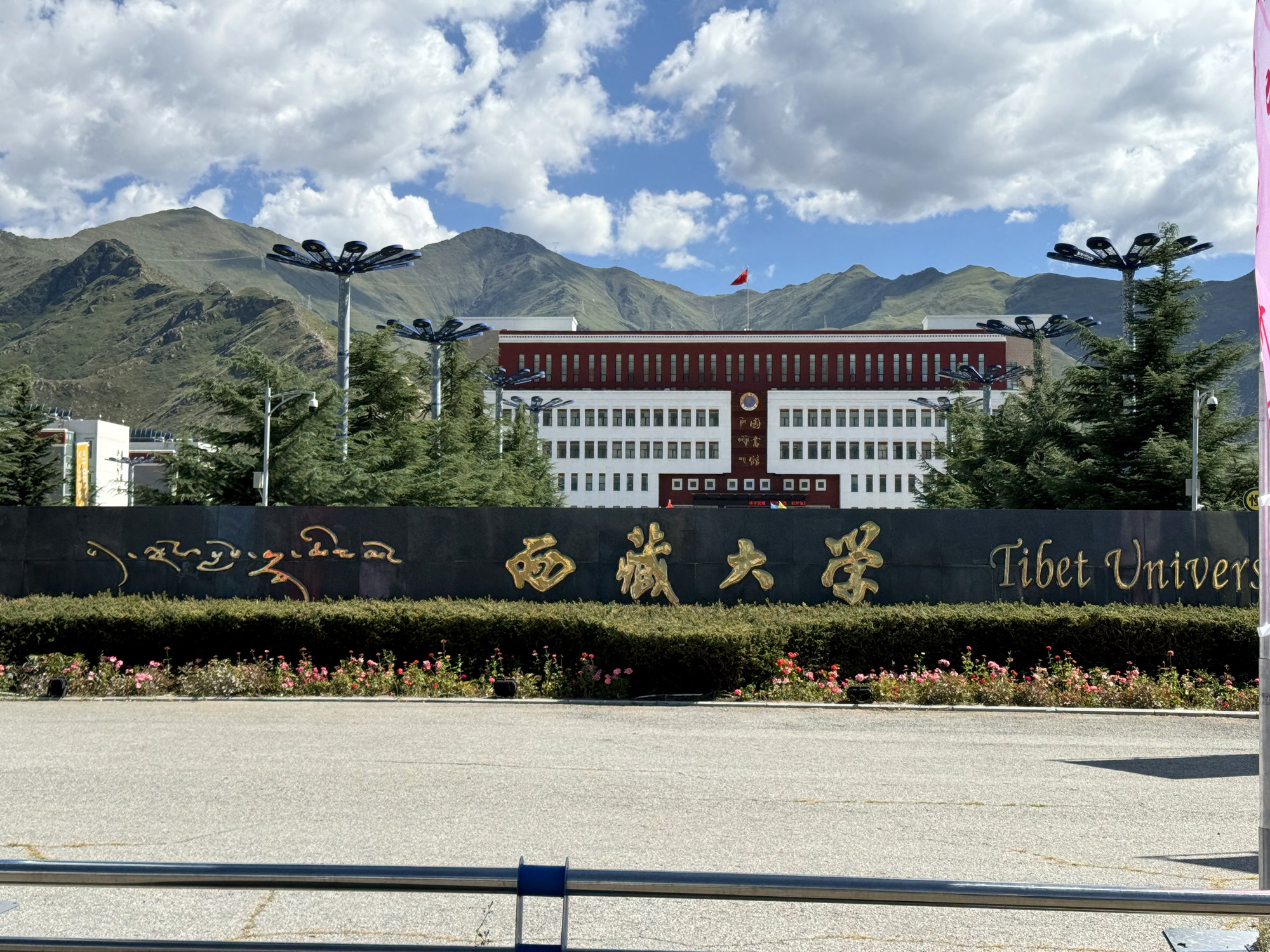 The Xizang University name wall, campus buildings, mountains, and white clouds