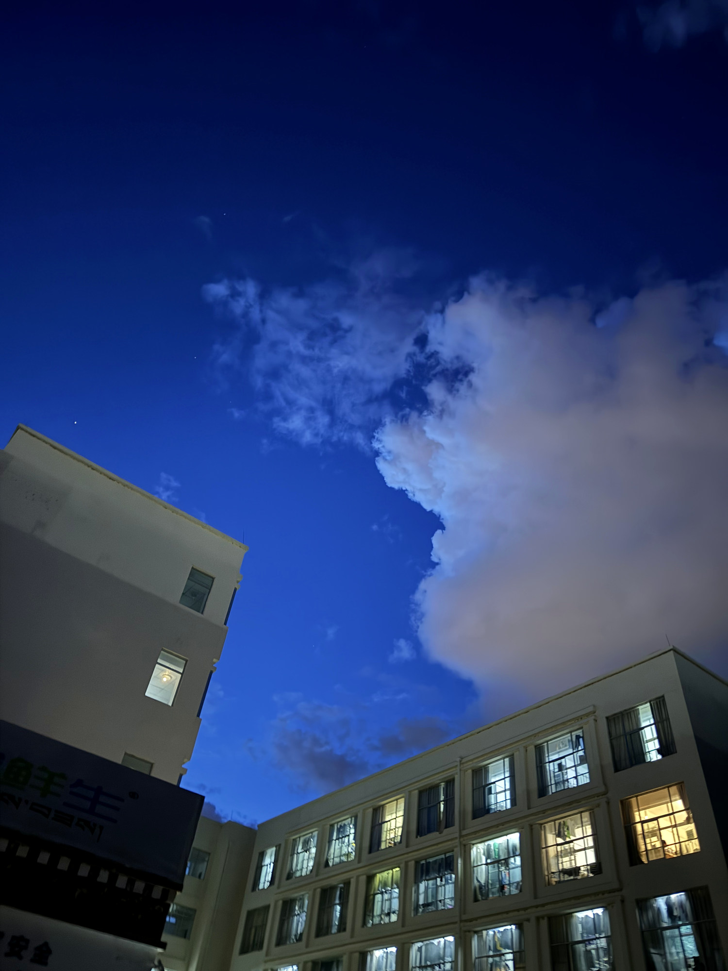 A deep-blue night sky, clouds, and illuminated campus buildings