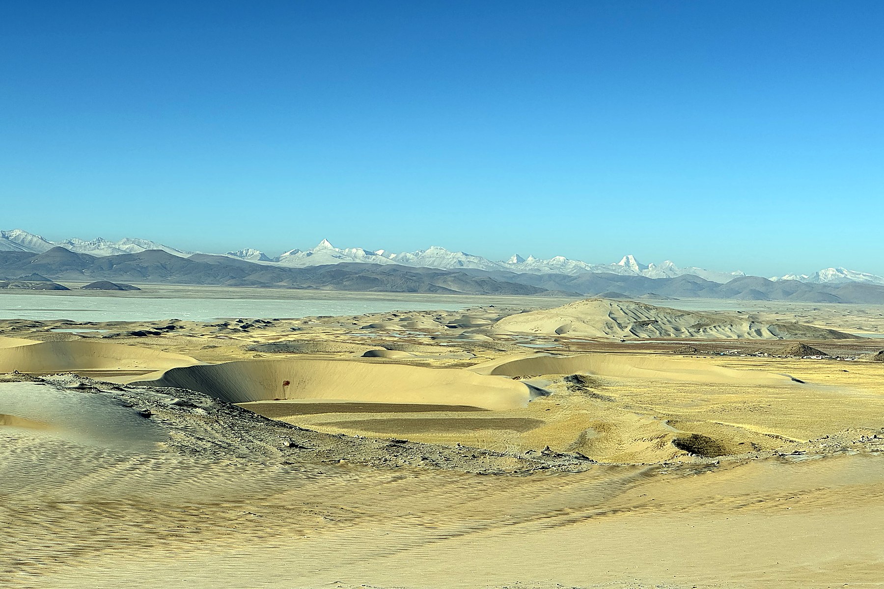 Pale winter dunes with snow-covered mountains in the distance