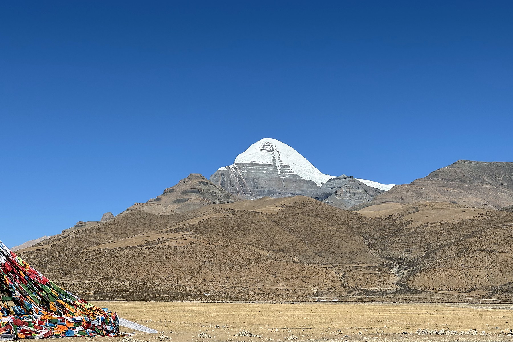 Mount Kailash beneath a blue sky, with prayer flags in the lower-left corner