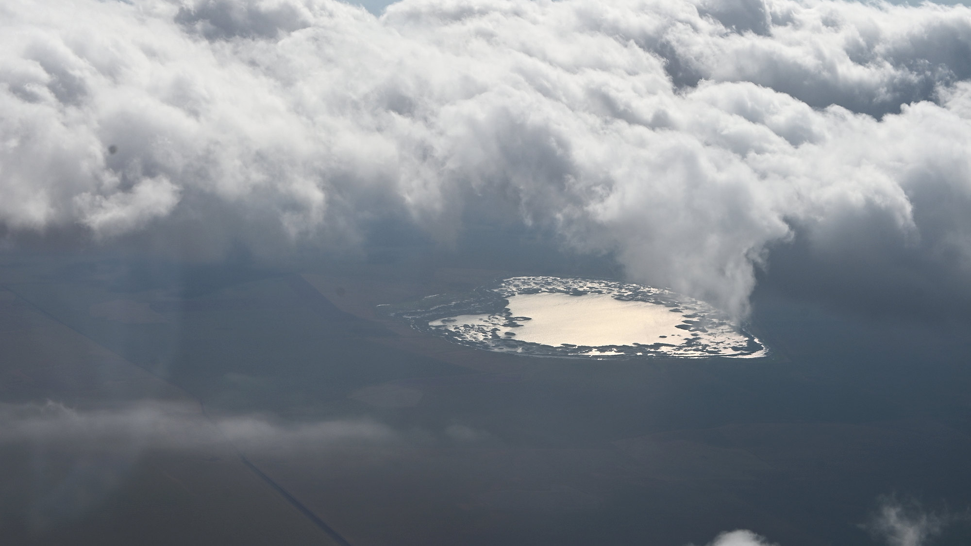 Clouds and a sunlit lake beneath the aircraft wing