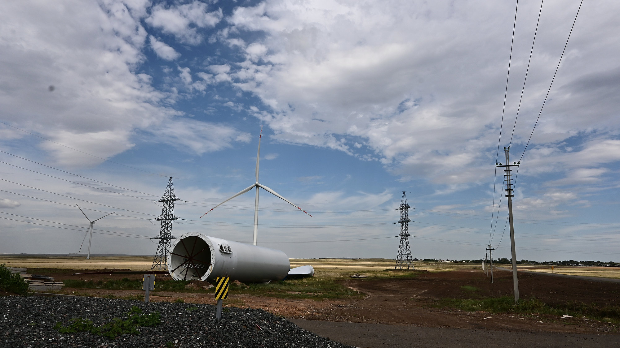 A tower section awaiting installation beside operating turbines and transmission infrastructure