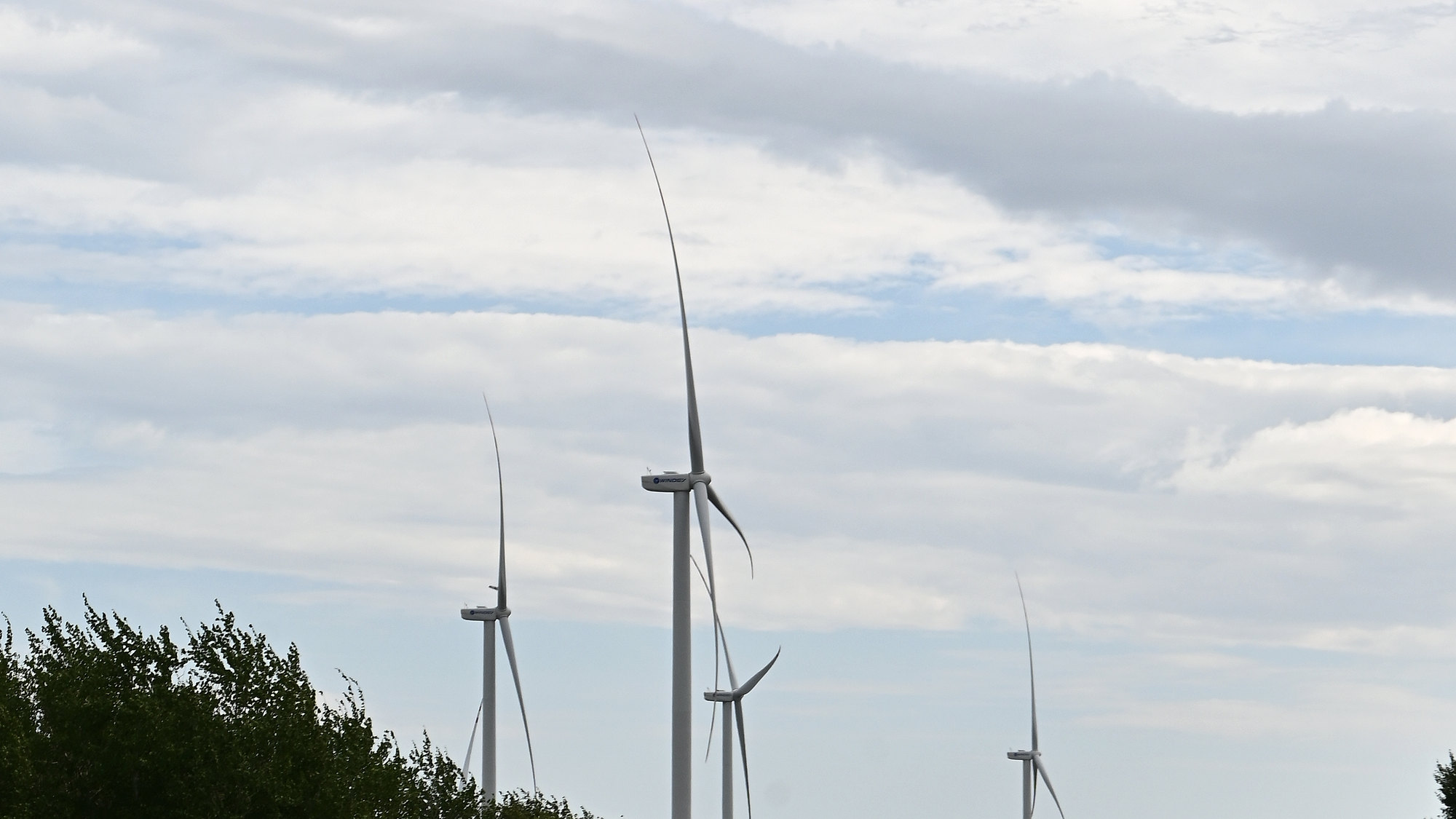 Several wind turbines standing across farmland beneath a layered sky