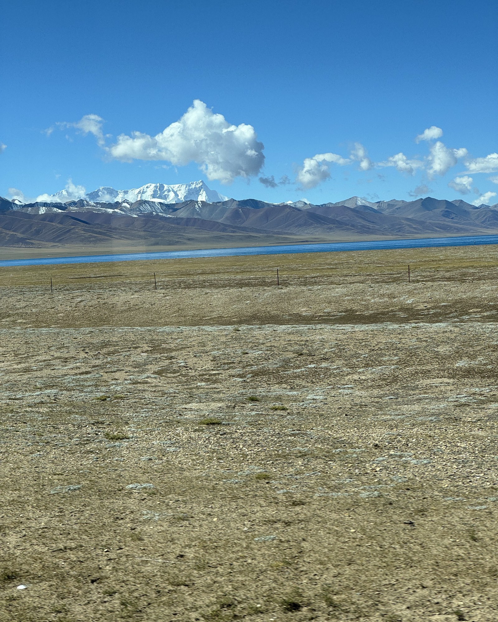 A blue band of Namtso beyond open ground, with snow-covered mountains in the distance