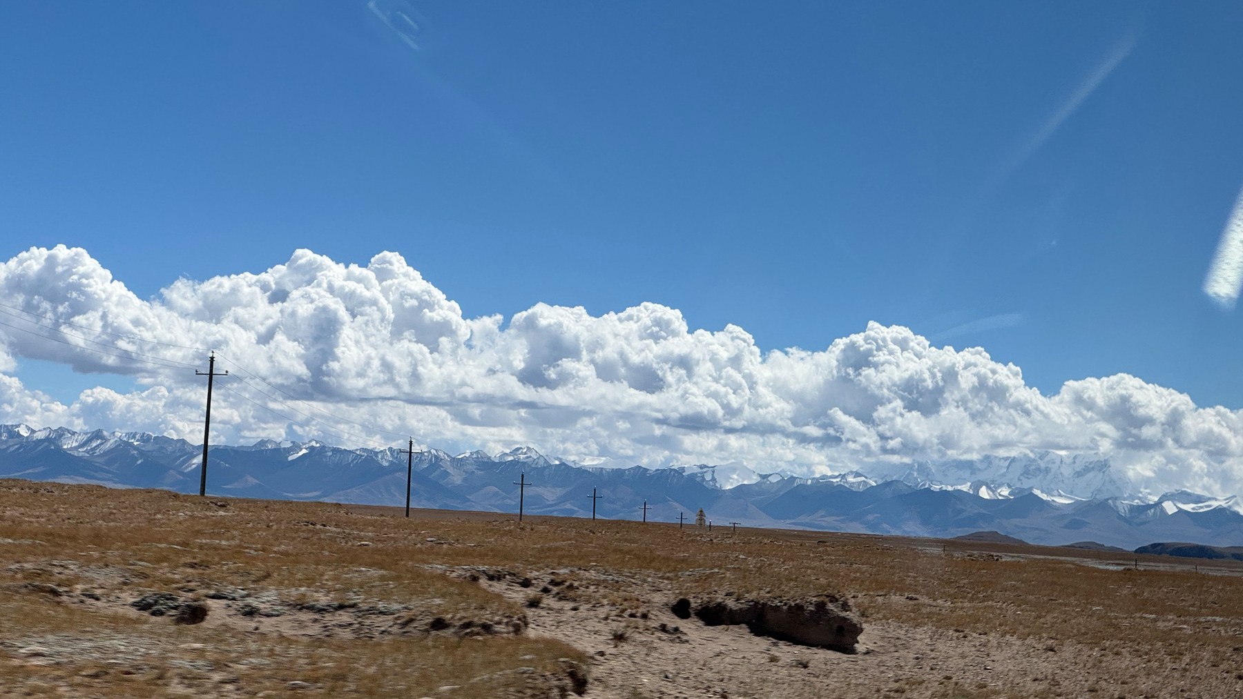 Utility poles crossing the plateau beneath clouds, with snow-covered mountains in the distance