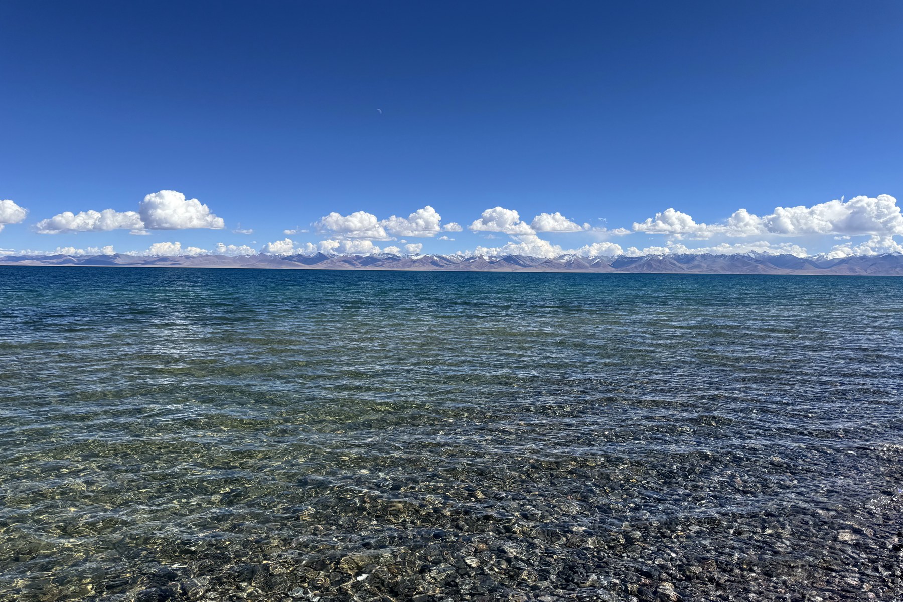 Clear lake water over near-shore gravel, with mountains spanning the horizon