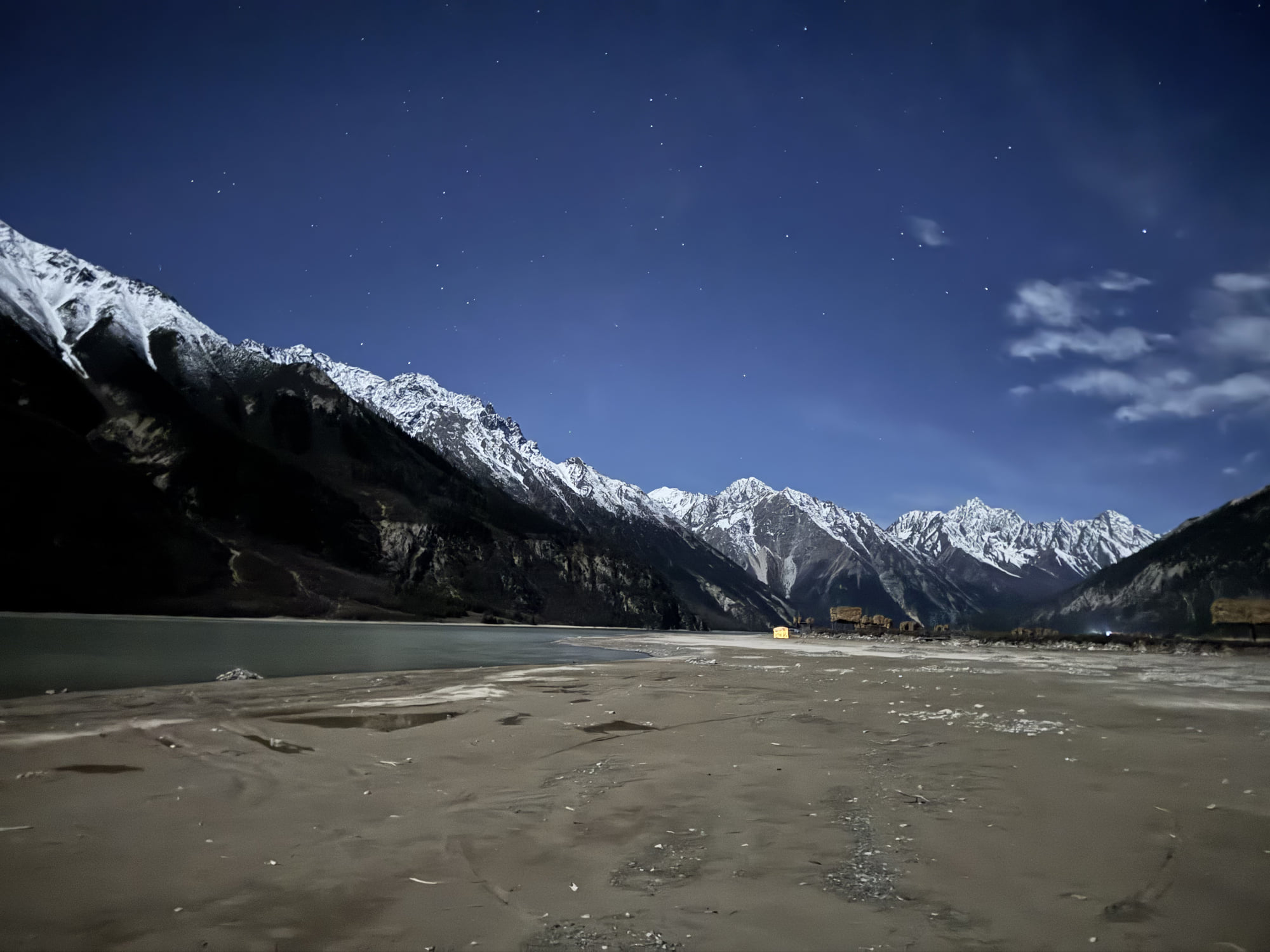 The lakeshore, stars, and a continuous line of snow-covered mountains at night