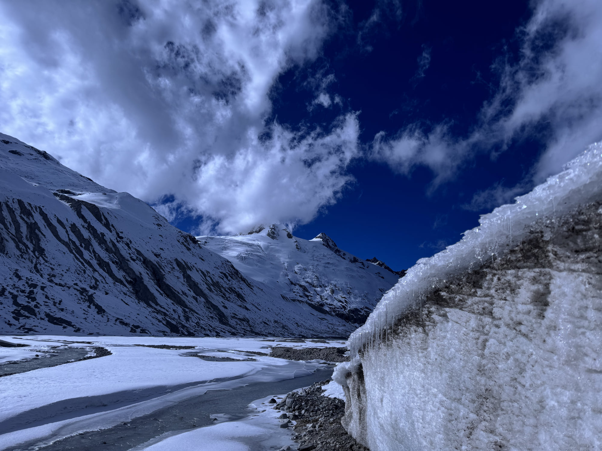 Snow-covered mountains, an ice wall, and frozen channels beneath cloud cover