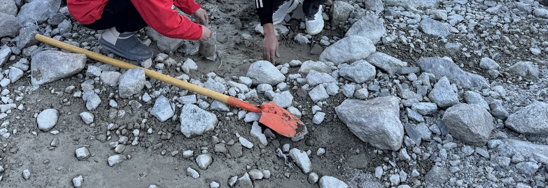 Hands and tools during two-person soil work on a gravel lakeshore