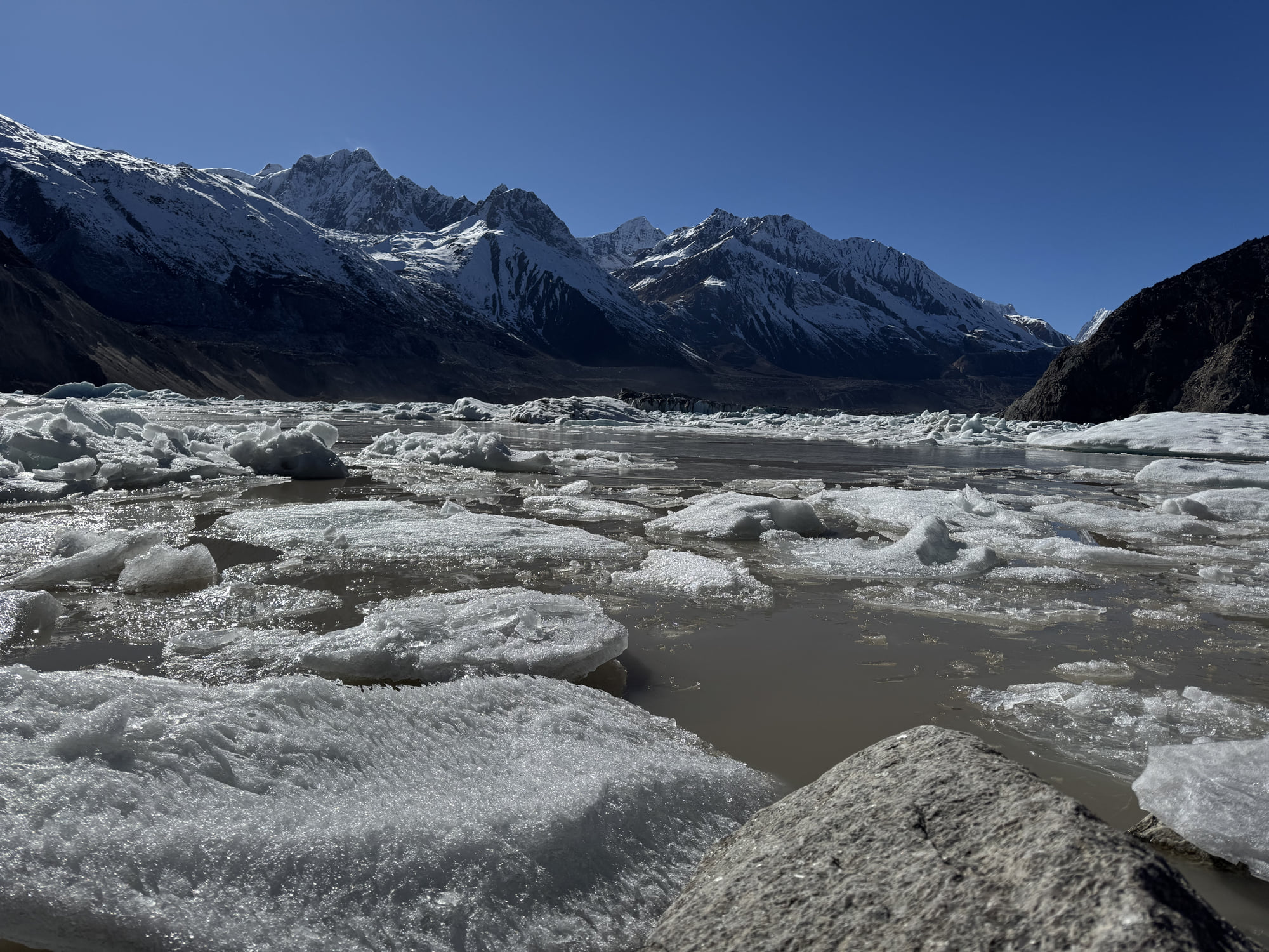 Broken ice across the lake with a continuous line of snow-covered mountains beyond