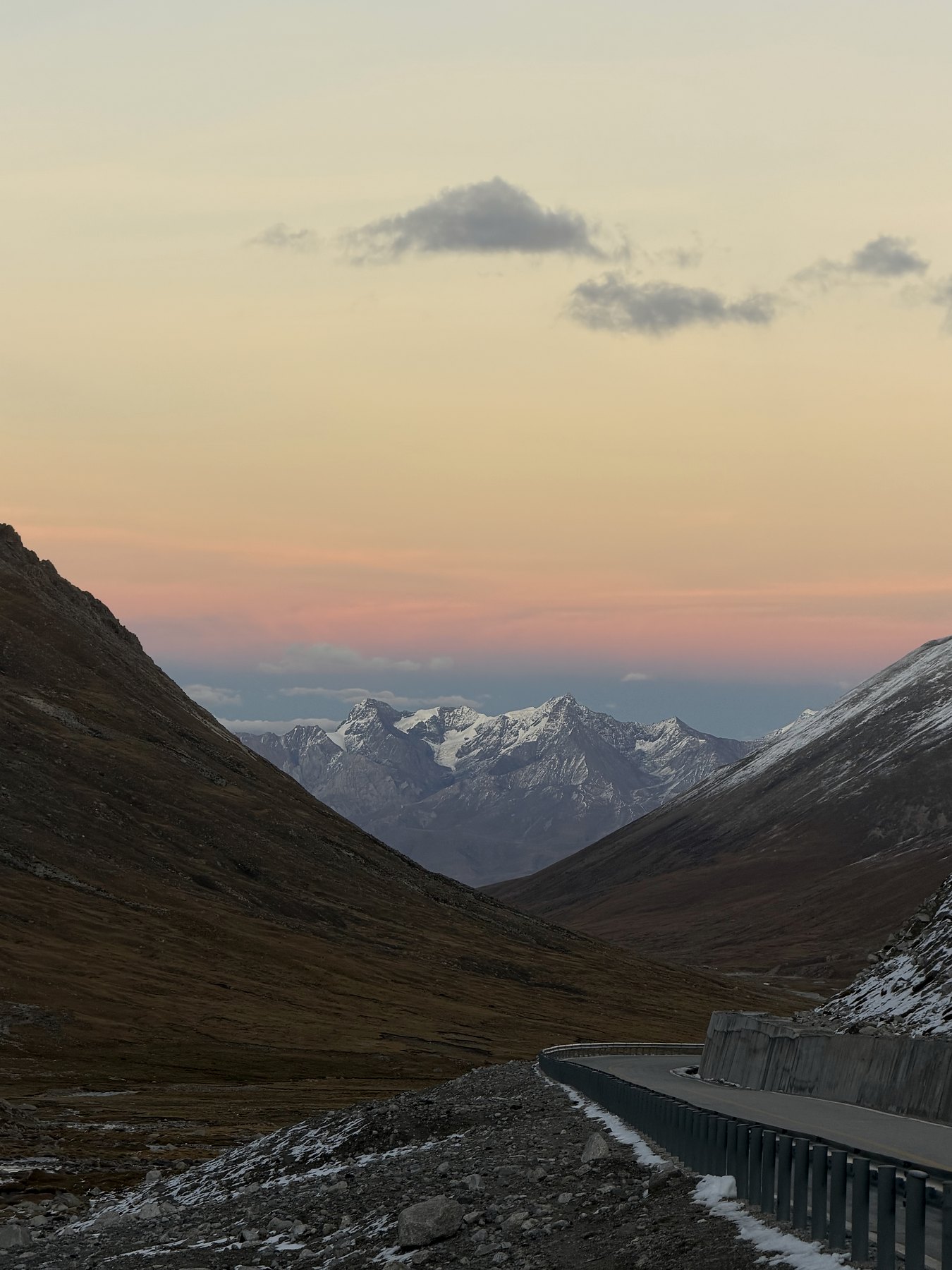 A high-altitude road running toward snowy mountains at dusk