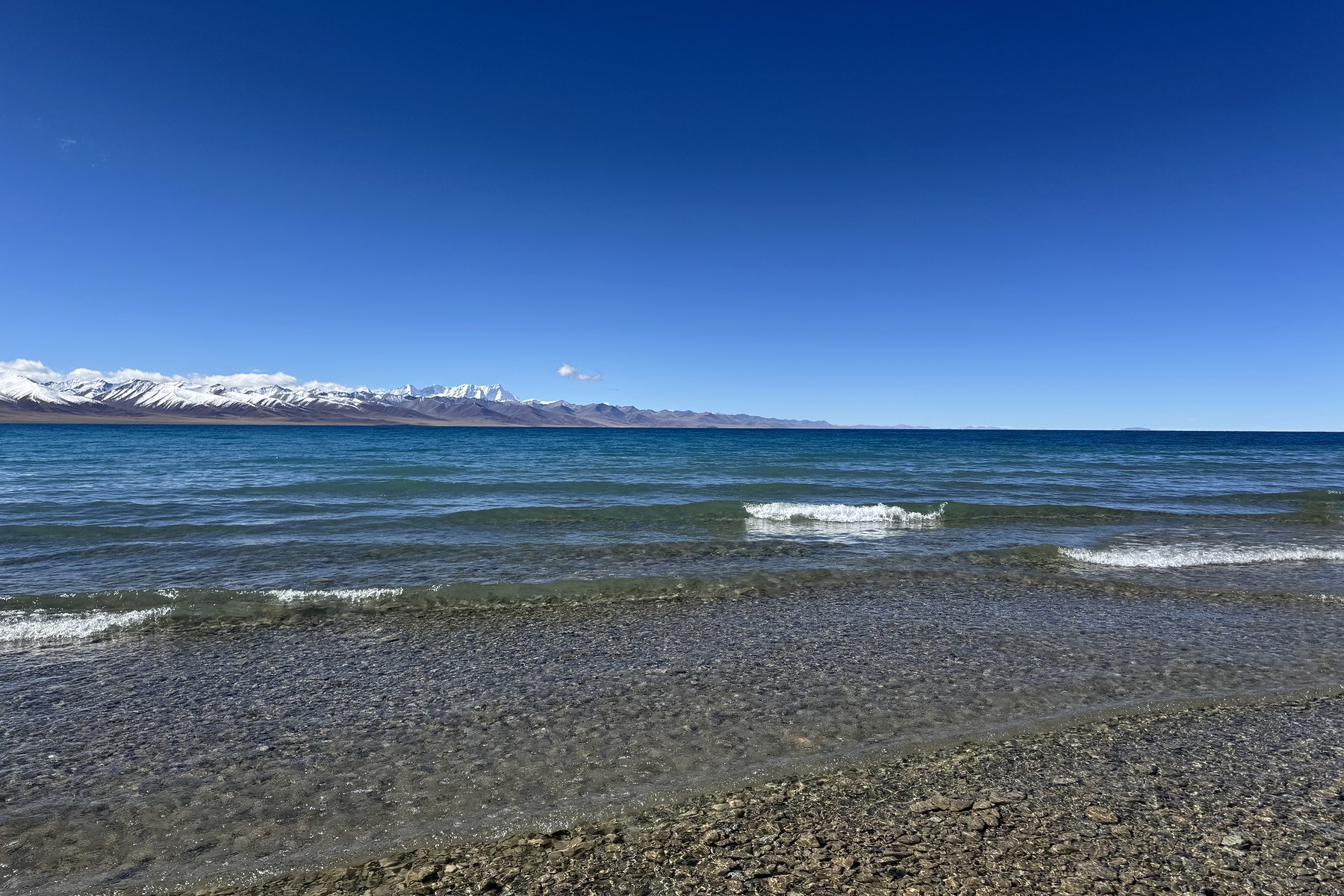Blue water, stones and distant mountains on the shore of Namtso